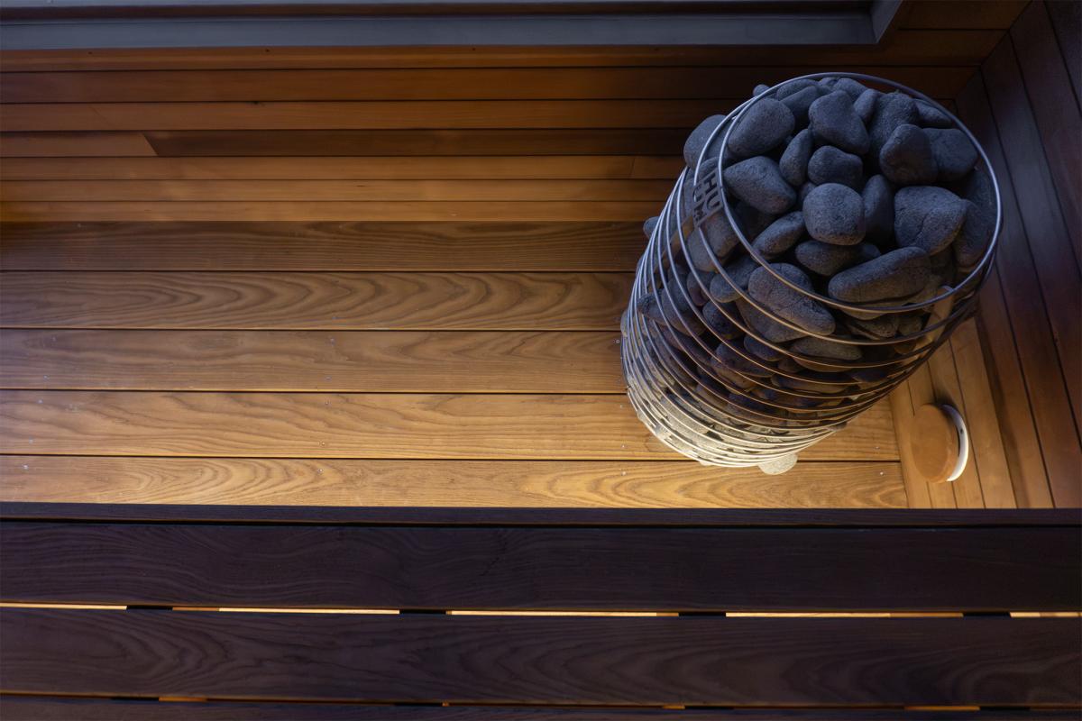 HUUM electric sauna heater beside wood flooring and a round wall vent inside the Ember Cabin
